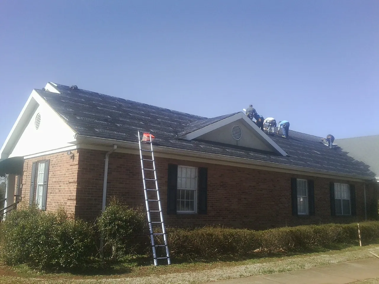 Crew tearing shingles off a brick ranch roof with a ladder set — Metal Roof Repair work by our crew in Hermitage