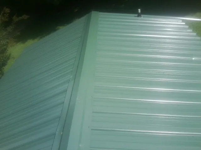 New green metal panels meeting at the ridge of a roof — Flat Roof Repair work by our crew in Hermitage